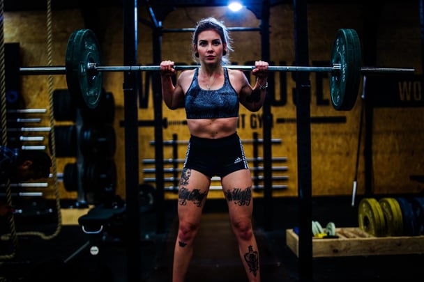 Woman with tattoos preparing to squat in gym